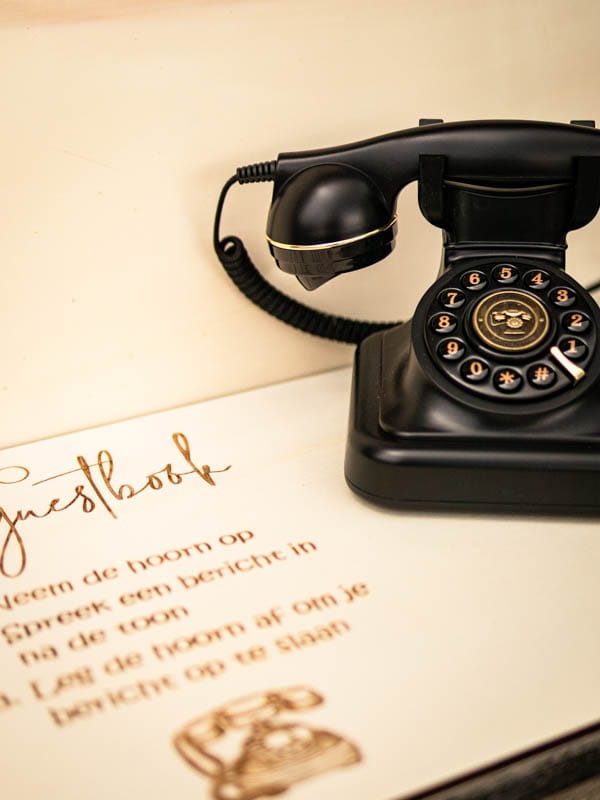 Zwarte retro telefoon met instructies voor het audioguestbook op een lichte ondergrond.