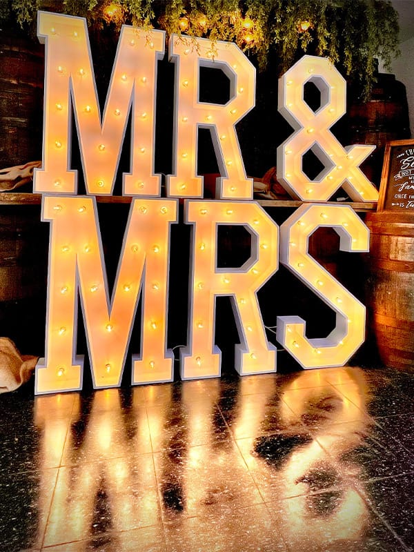 Grote verlichte MR & MRS lichtletters in een rustieke setting met houten vaten en groen decor.