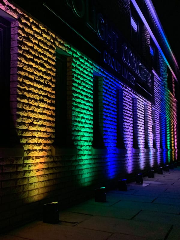 Gekleurde uplights die een bakstenen gevel verlichten in een verloop van geel tot paars.