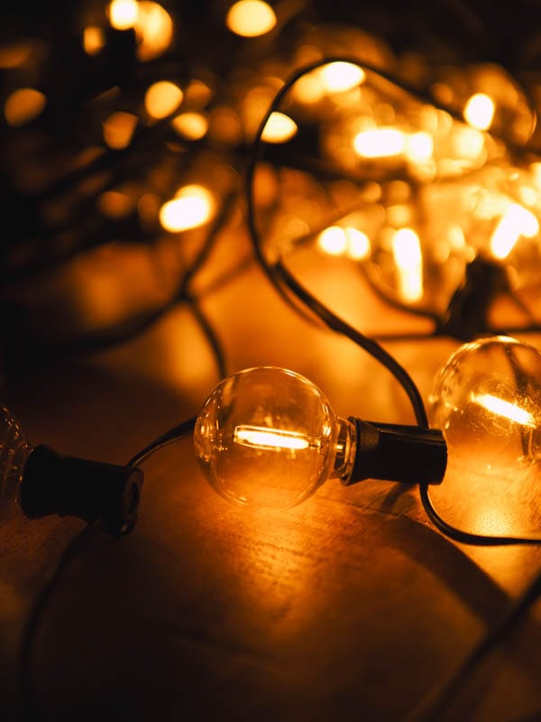 Warmgele sfeerlampjes op een houten oppervlak, deels brandend en verbonden met zwarte kabels.