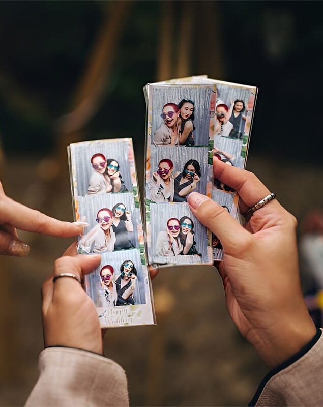 Handen die fotostrips vasthouden met vrolijke foto’s van gasten voor een feestelijke backdrop.